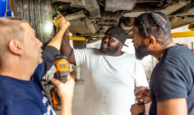 Students inspecting vehicle under lift during automotive vocational training program